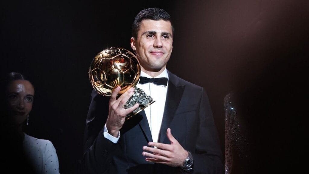 Rodri holding the Ballon d'Or 2024 award in a suit